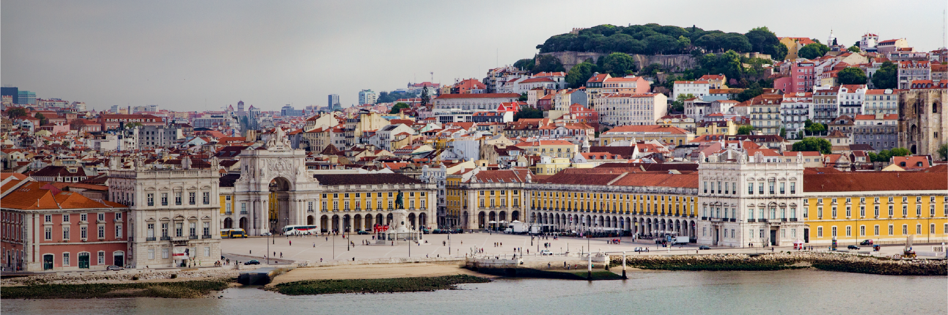 Cityscape of Lisbon’s main riverside square, Praça do Comércio, showing a large archway (Arco da Rua Augusta), classical-style buildings, and the Tagus River in the foreground.